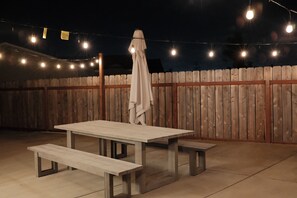 An outdoor patio with a picnic table and benches, surrounded by a wooden fence and string lights. - Modern SD Home / Sleeps 6 / Fast WiFi / Beach within 10 miles / Games + BBQ (San Diego)