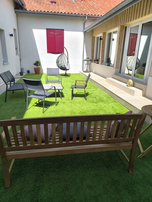 A patio with artificial grass, a wooden bench, and outdoor furniture.