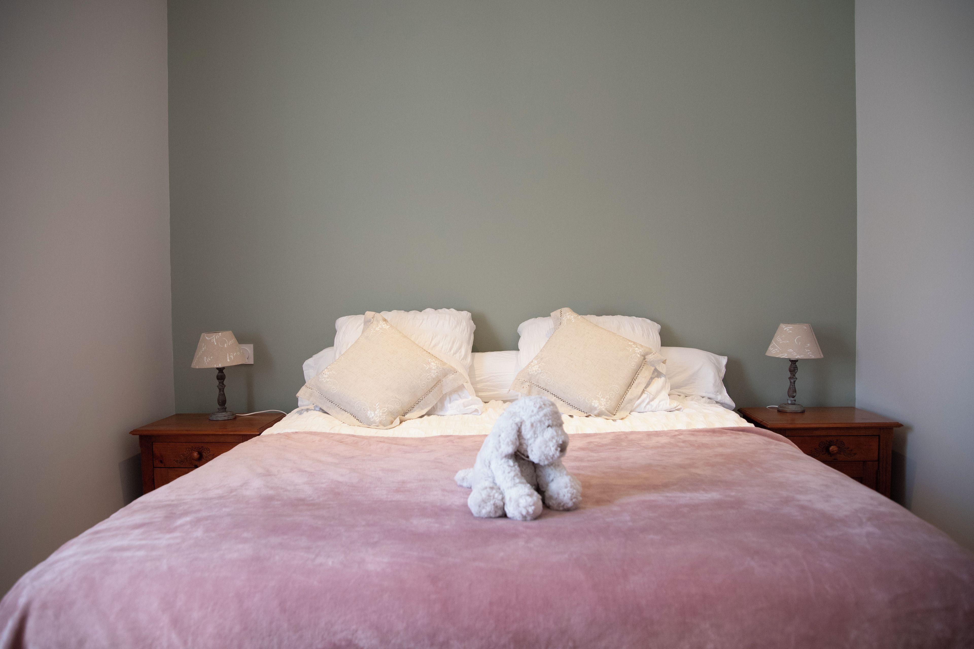 Una cama bien hecha con una colcha rosa y dos lámparas de noche sobre mesitas de madera.