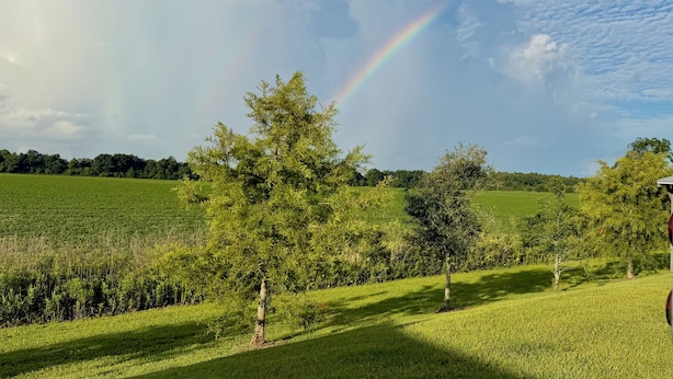 A rural landscape with a rainbow, trees, and open fields. - RV Resort, Back-In Full Hookup, 3 Pools, Snowbirds, Kids, Pets (Foley)