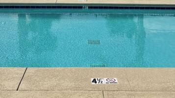 A swimming pool with lounge chairs and palm trees, surrounded by a fence.