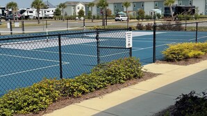 A fenced parking area with a basketball court, a sign indicating a reserved parking spot, and a building in the background. - RV Resort, Back-In Full Hookup, 3 Pools, Snowbirds, Kids, Pets (Foley)