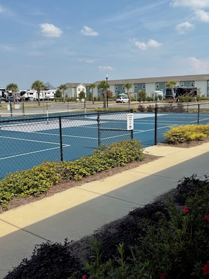 A fenced parking area with a basketball court, a sign indicating a reserved parking spot, and a building in the background. - RV Resort, Back-In Full Hookup, 3 Pools, Snowbirds, Kids, Pets (Foley)