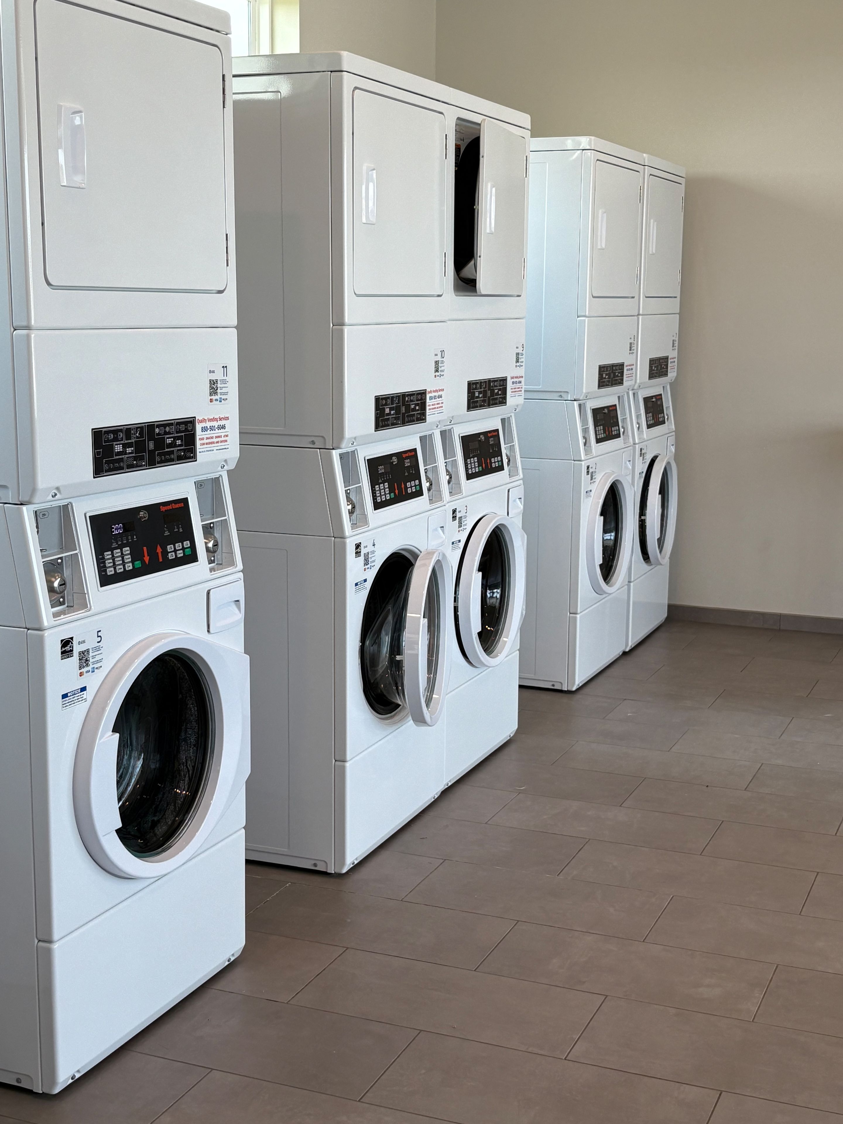A row of stacked front-loading washing machines in a commercial laundry room.