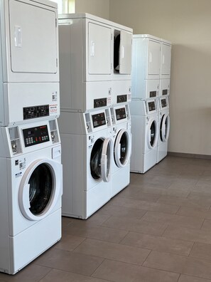 A row of stacked front-loading washing machines in a commercial laundry room.