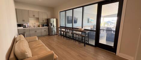 A spacious living area with a sofa, a dining table with chairs, a kitchen with cabinets and appliances, and a large sliding glass door leading to an outdoor area.