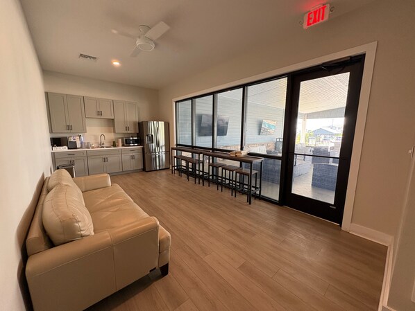 A spacious living area with a sofa, a dining table with chairs, a kitchen with cabinets and appliances, and a large sliding glass door leading to an outdoor area.