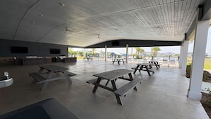 An outdoor covered patio area with picnic tables and seating. - RV Resort, Back-In Full Hookup, 3 Pools, Snowbirds, Kids, Pets (Foley)