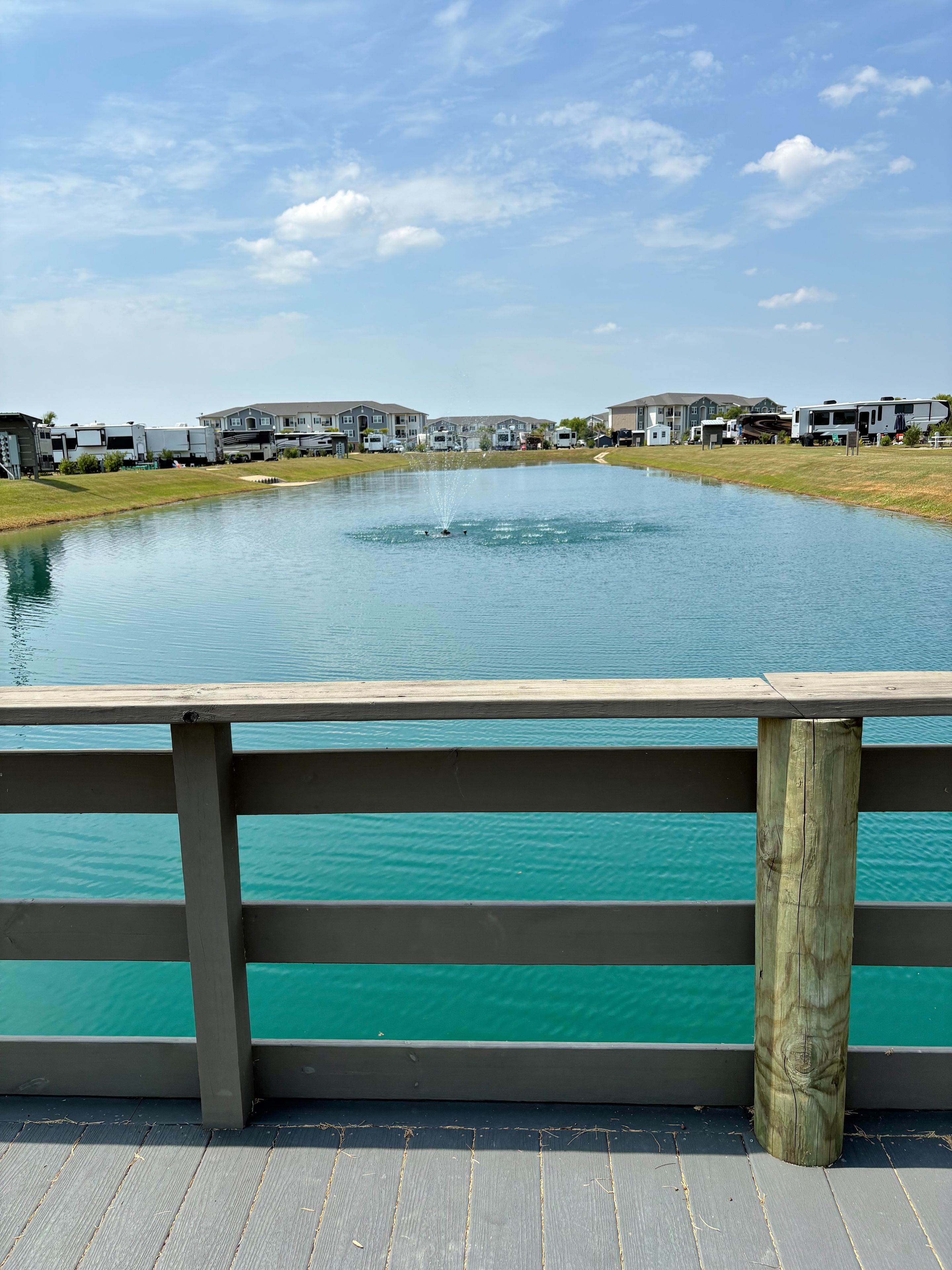 A waterfront view with a wooden deck, a pond, and RVs in the background.
