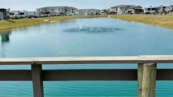 A waterfront view with a wooden deck, a pond, and RVs in the background.
