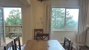 A dining area with a chandelier, a large table, and chairs. There are windows with curtains, and a view of trees outside. - Cozy 3-bed mtn condo in village, walkable to all! (Slaty Fork)