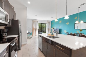A modern kitchen with a large island, stainless steel appliances, and a teal accent wall. - New Domani Resort Escape | Minutes to Disney (Davenport)