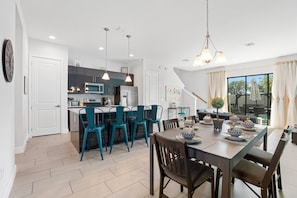 A modern kitchen with a central island, dining area with chairs, and a large window with curtains. - New Domani Resort Escape | Minutes to Disney (Davenport)