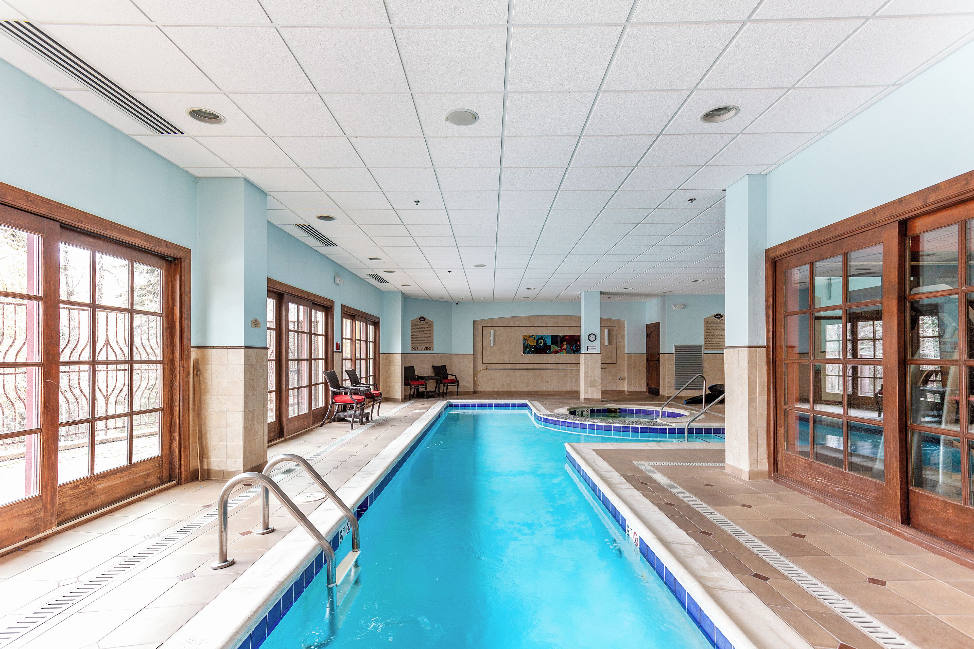 Une piscine intérieure à l’eau claire, entourée de murs carrelés et de fenêtres à cadre en bois.