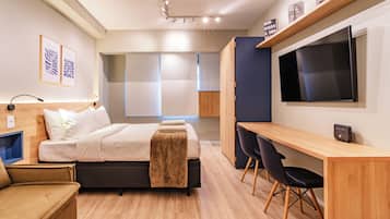 Moderni hotellihuone, jossa on sänky, yöpöytä, työpöytä, tuoleja ja televisio.