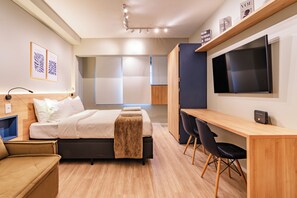 Ein modernes Hotelzimmer mit Bett, Nachttisch, Schreibtisch, Stühlen und einem Fernseher.