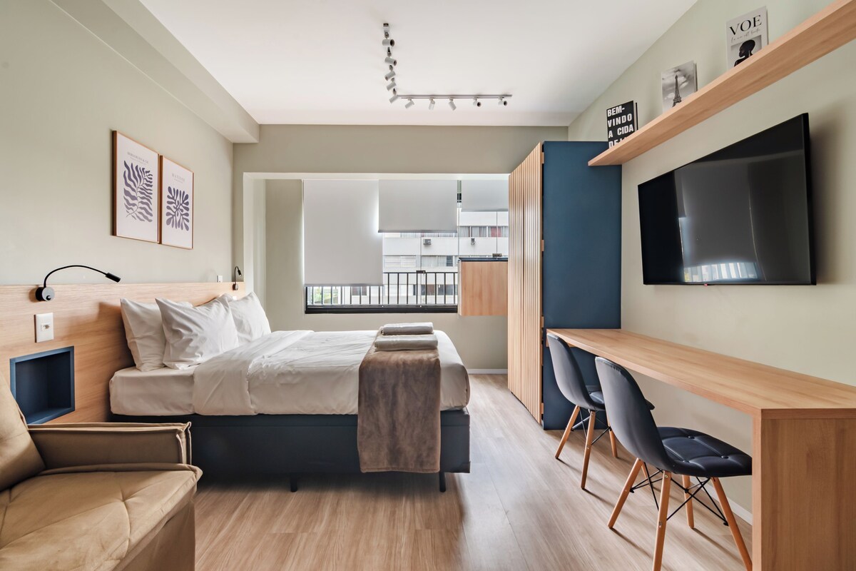 Ein modernes Hotelzimmer mit Bett, Schreibtisch, zwei Stühlen, Fernseher und Wandbild.