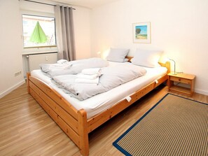 A single bed with a wooden frame, a bedside table with a lamp, a window with curtains, and a framed picture on the wall. - Flurstrasse 10, Holiday Apartment 1 (Wyk auf Foehr)