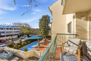 Ein Balkon mit Pool, Liegestühlen und Blick auf eine Straße sowie Gebäude.