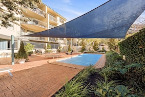 A swimming pool area with a shaded canopy, potted plants, and a brick pathway. - Stylish 2-bed Apartment in Kingston (Canberra)