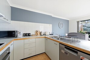 Eine moderne Küche mit weißen Schränken, einer Mikrowelle, einer Kaffeemaschine und einem Spülbecken.