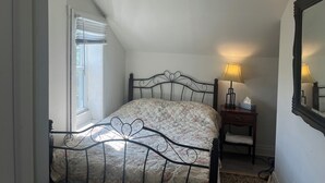 A bedroom with a bed, a bedside lamp, a nightstand, a window with blinds, and a ceiling light fixture. - Charming 4-bedroom building with AC in peaceful Cramahe (Cramahe)
