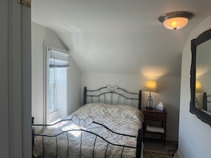 Une chambre à coucher comprenant un lit, une lampe de chevet, une table de chevet, une fenêtre avec des stores et un luminaire au plafond.
