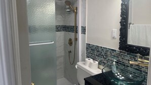 A bathroom with a glass-enclosed shower, a toilet, and a sink with a glass basin. - Charming 4-bedroom building with AC in peaceful Cramahe (Cramahe)