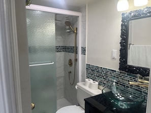 Une salle de bain dotée d’une douche à parois de verre, de toilettes et d’un lavabo avec un récipient en verre.
