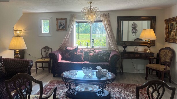 A living room with a sofa, chairs, a table, a chandelier, and a window with curtains. - Charming 4-bedroom building with AC in peaceful Cramahe (Cramahe)