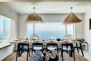 A dining area with a table set for four, overlooking a body of water. - Camps Bay 6 Bed Ocean Views and Pool Villa Kai (Cape Town)