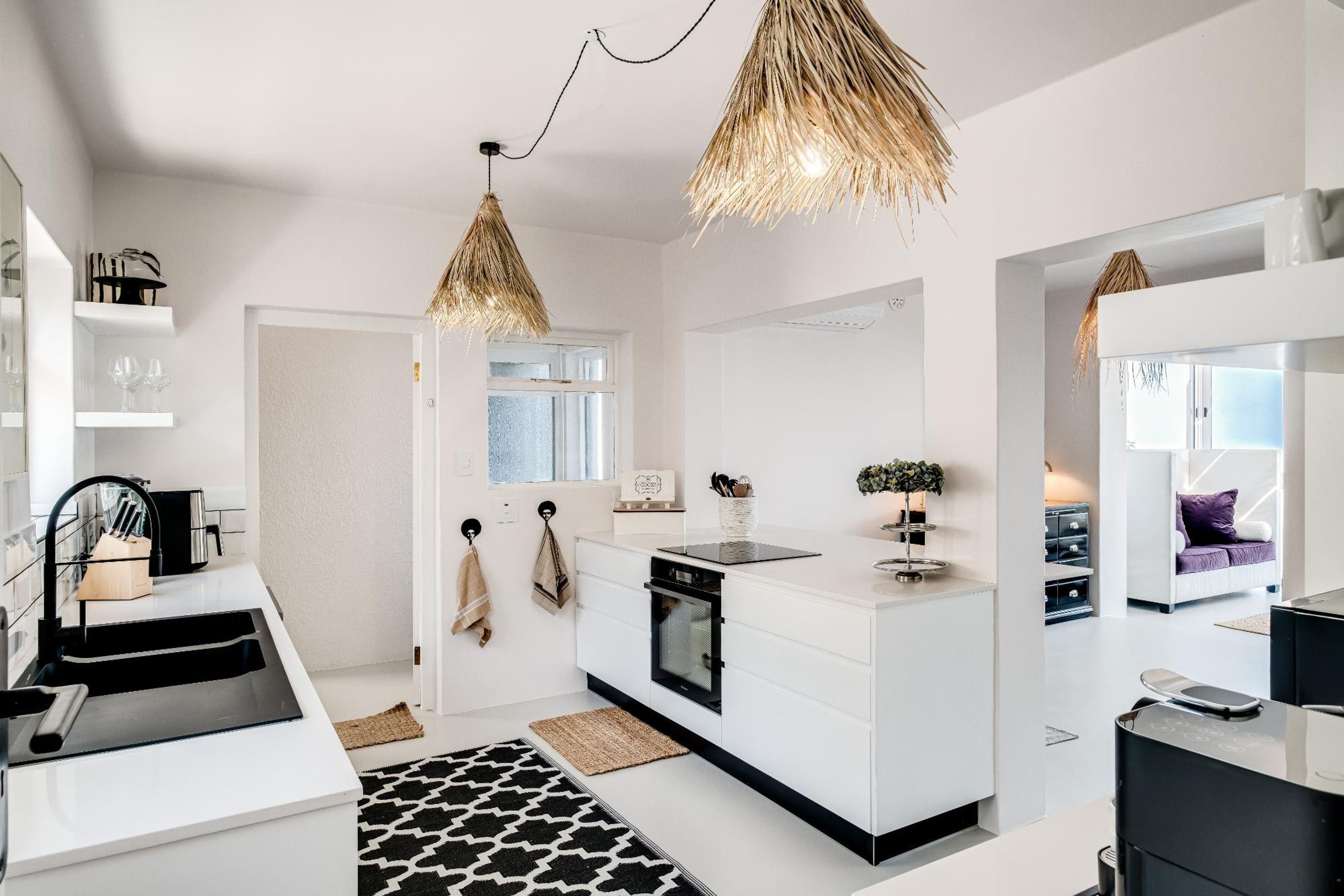 A modern kitchen with white cabinetry, a black countertop, and a hanging light fixture. - Camps Bay 6 Bed Ocean Views and Pool Villa Kai (Cape Town)