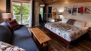 Um quarto acolhedor com teto de madeira, cama com roupa de cama floral, sofá com almofadas estampadas e um banquinho.
