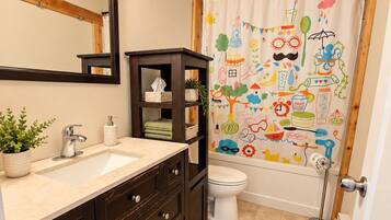 A bathroom with a wooden ceiling, a large mirror, a dark wooden vanity, a white toilet, and a colorful shower curtain.