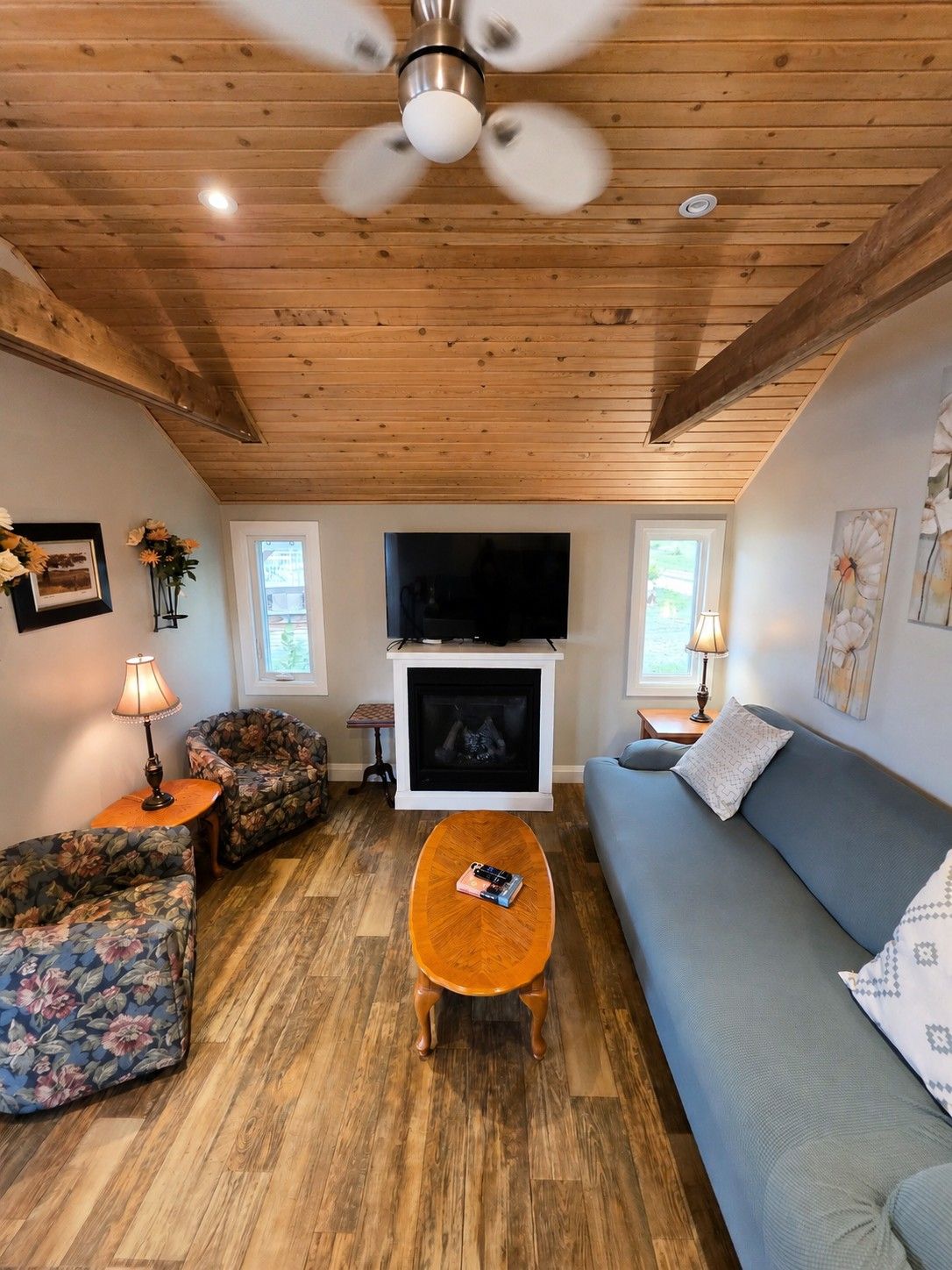 A living room with a fireplace, a ceiling fan, and a television.