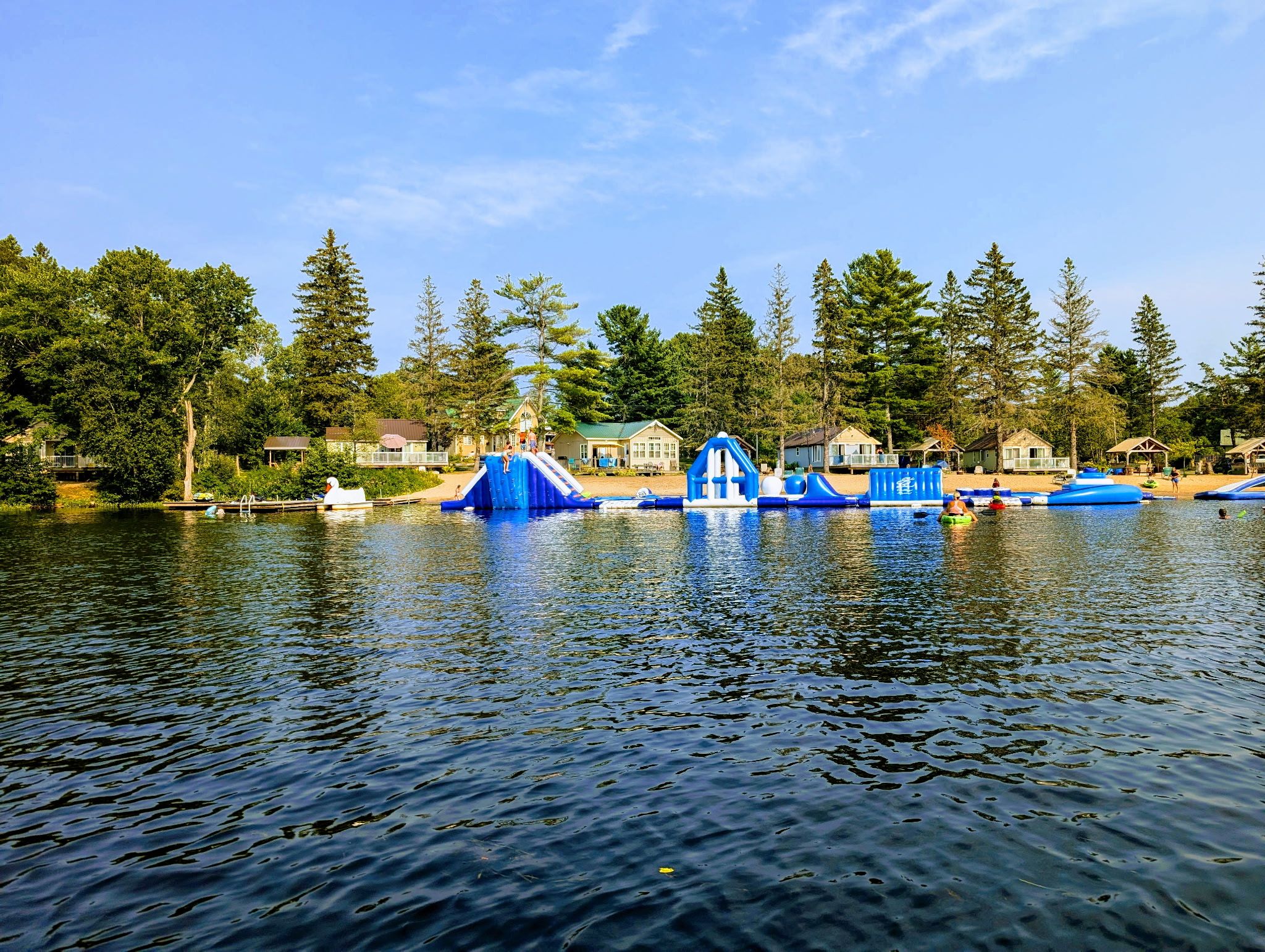 A lakeside view with a dock, inflatable slides, and cabins.