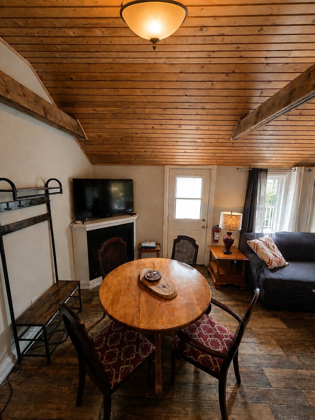 A cozy living room with a wooden ceiling, a round wooden table, and a black leather sofa.