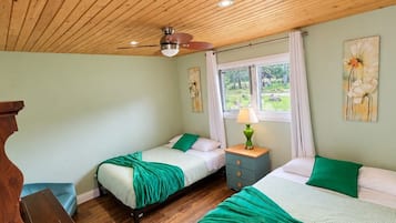A room with two beds, a wooden ceiling, a window with curtains, and a wooden desk.