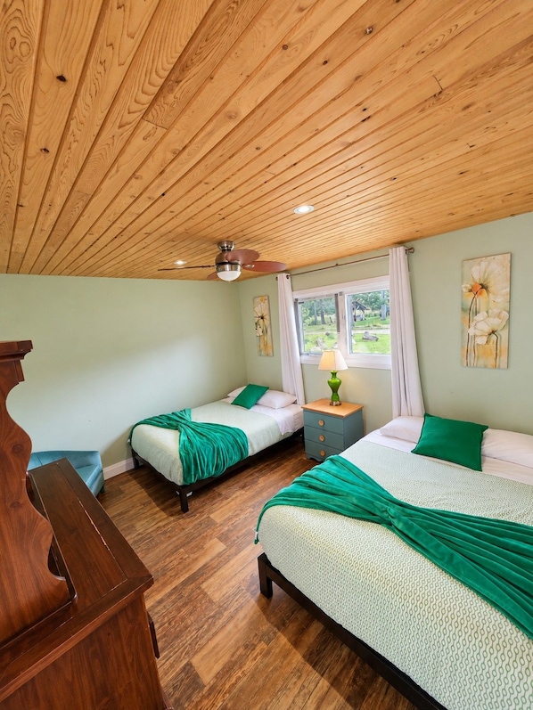 A room with two beds, a wooden ceiling, a window with curtains, and a wooden desk. - Echo Beach Cottage Resort (Magnetawan)