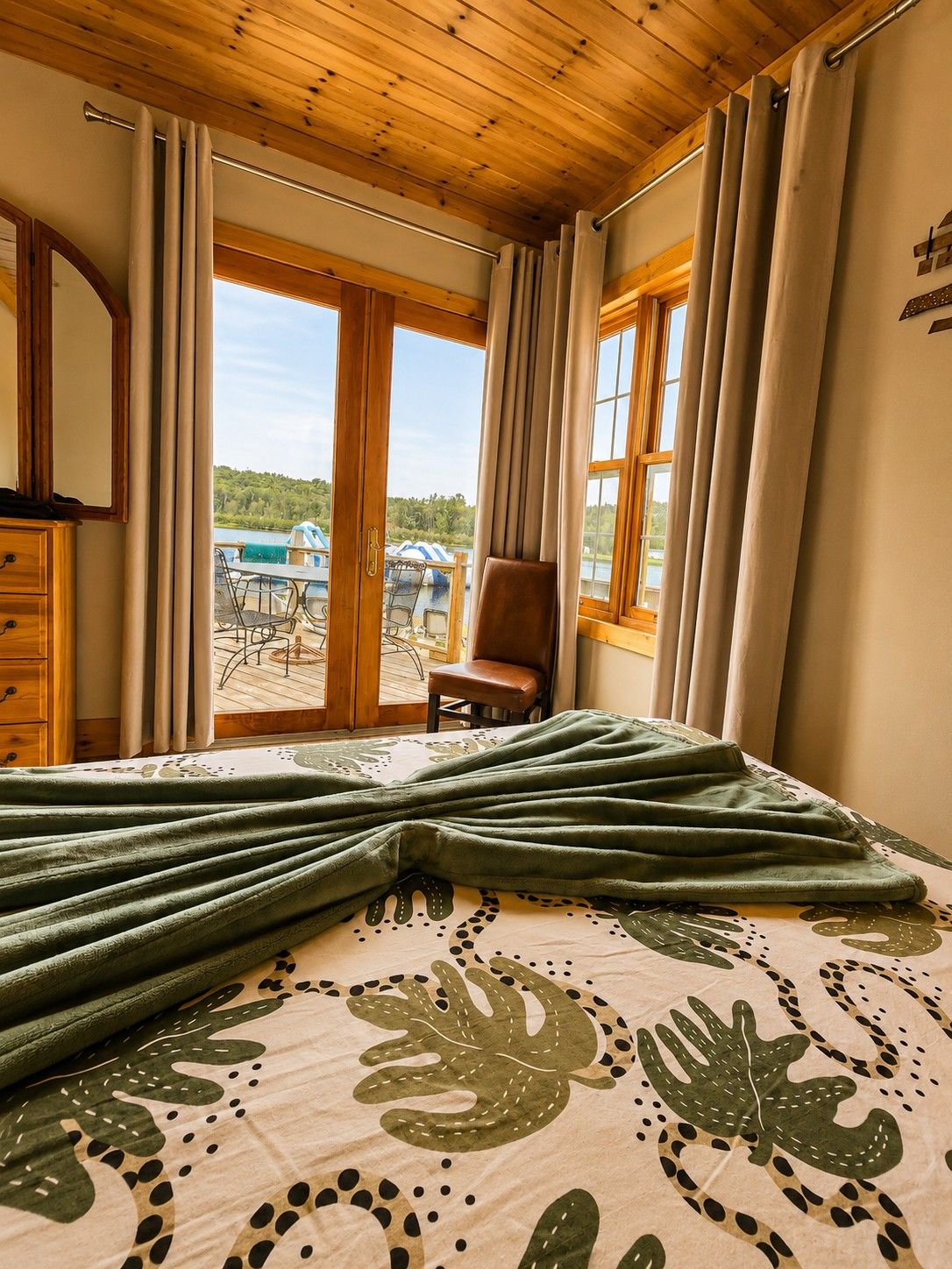A room with a bed, a chair, and a view of a lake with boats.