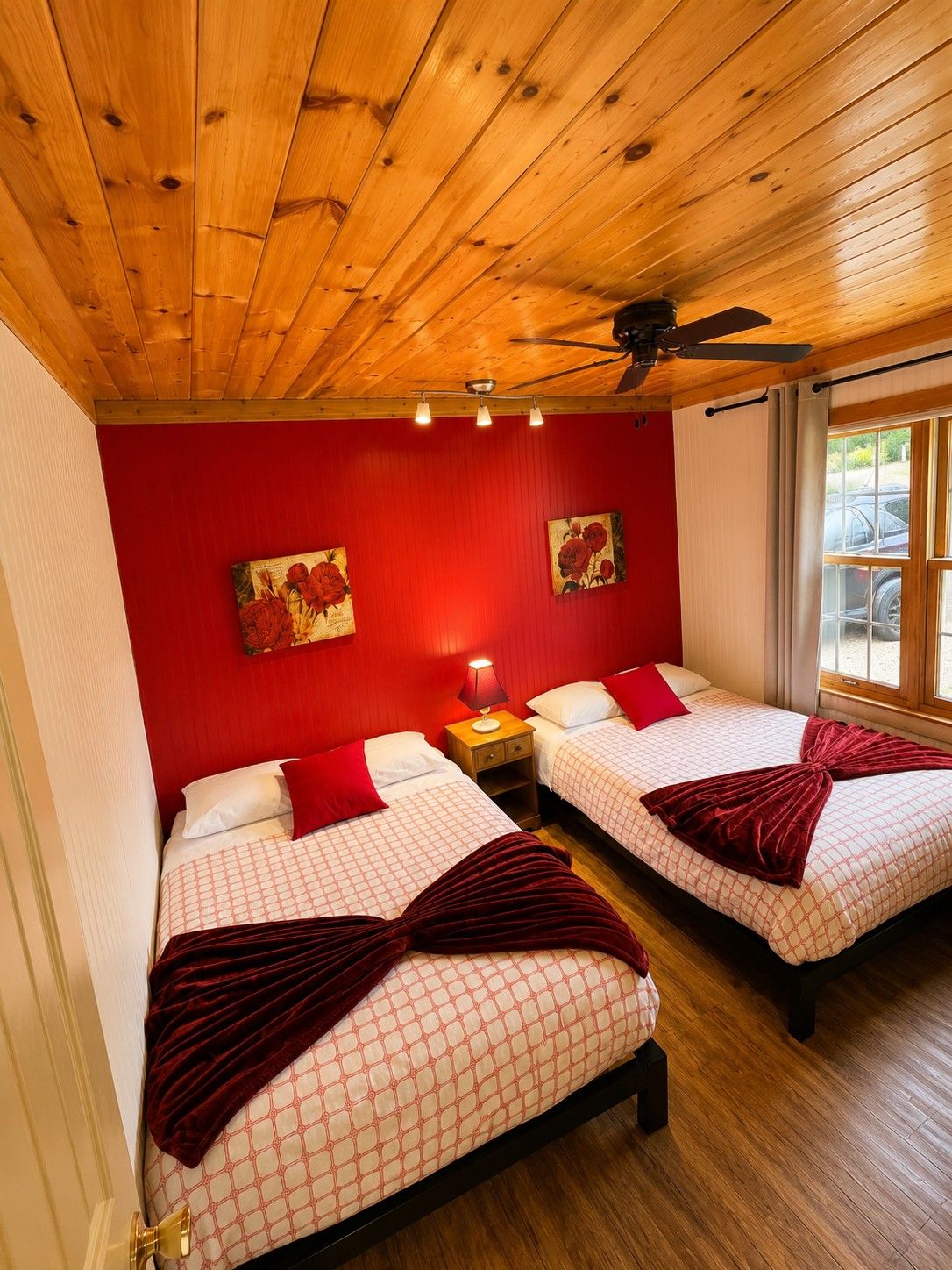 A room with two beds, red walls, wooden ceiling, and a window with a view.