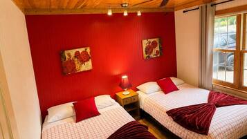 A room with two beds, red walls, wooden ceiling, and a window with a view.