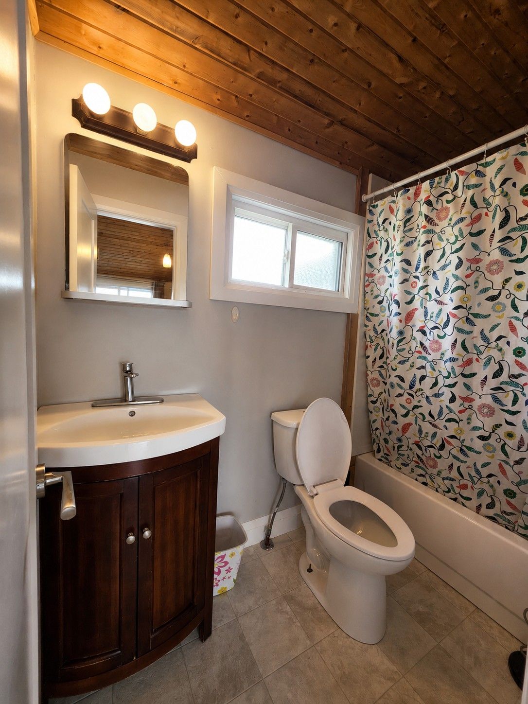 A bathroom with a wooden ceiling, a white sink, a toilet, and a shower curtain with a floral pattern.