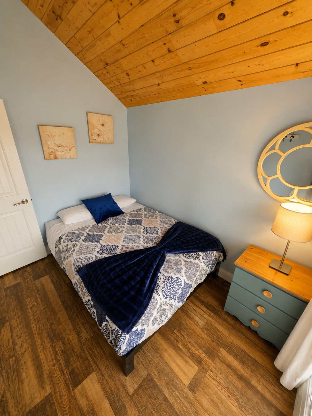 A bedroom with a bed, a nightstand, a lamp, and two wall art pieces.