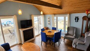 A spacious living area with a wooden ceiling, a dining table with blue chairs, a sofa, and a television.