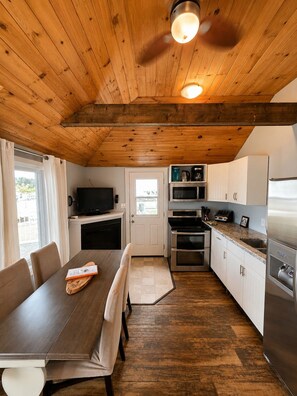 A modern kitchen with wooden ceiling beams, a dining table with chairs, and a built-in oven. - Echo Beach Cottage Resort (Magnetawan)