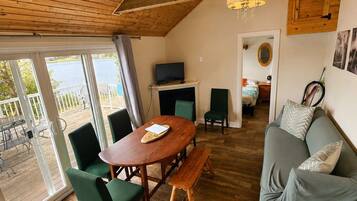 A cozy living room with a wooden ceiling, a fireplace, a sofa, and a dining table with chairs.