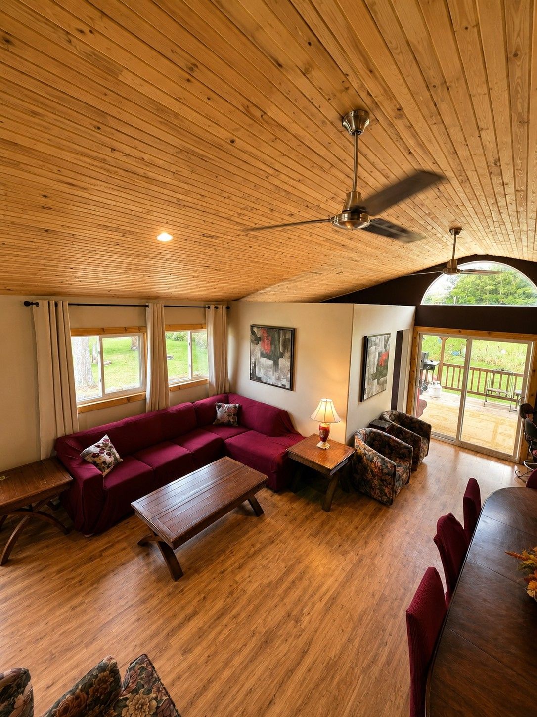 A spacious living room with a wooden ceiling, a red sofa, a coffee table, and a dining area with a table and chairs.