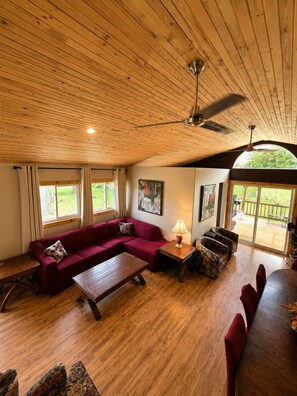 A spacious living room with a wooden ceiling, a red sofa, a coffee table, and a dining area with a table and chairs. - Echo Beach Cottage Resort (Magnetawan)