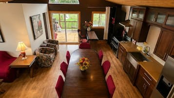 A spacious dining area with a wooden table and red chairs, a kitchen with modern appliances, and a view of a wooden deck through large windows.